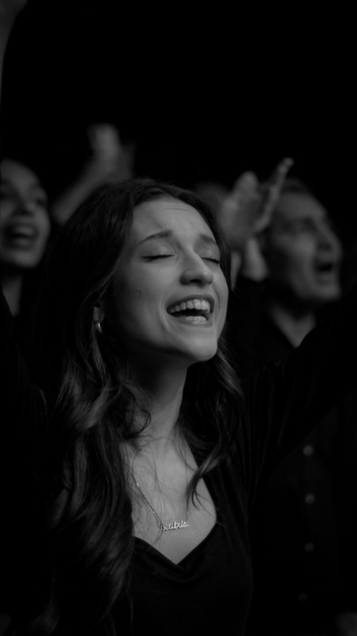 Black and white photo of a woman singing and enjoying a live music concert surrounded by others.